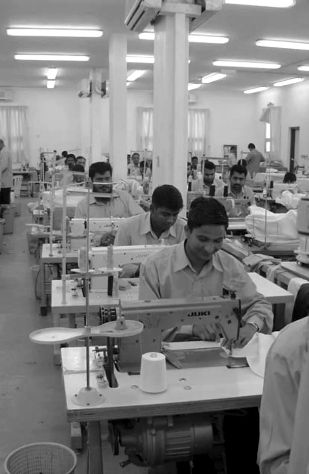 A machinist at an industrial sewing machine, colleagues working behind